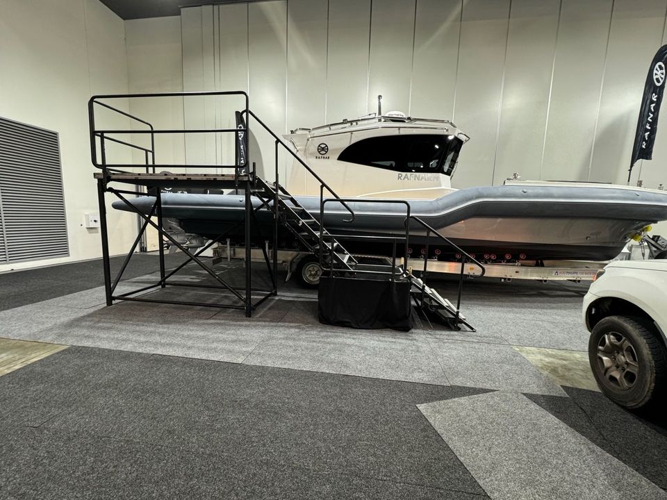 Boat on a raised black frame display stage with stairs and handrails in an exhibition hall