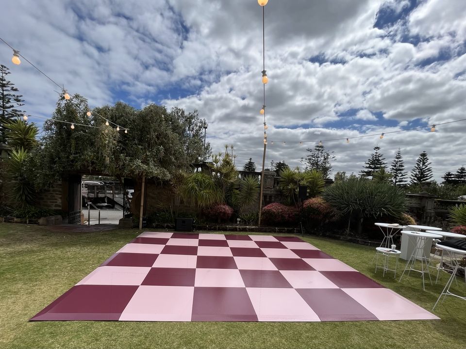 Pink and maroon checkered dance floor on a lawn under festoon lights