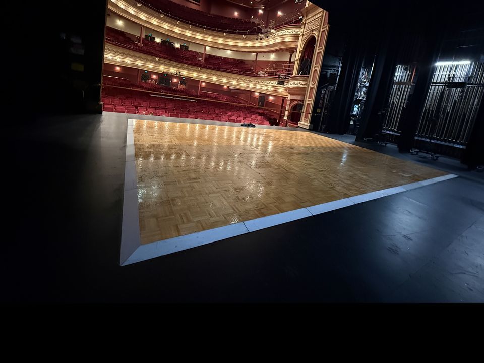Parquetry dance floor with white edging on a theatre stage, facing the tiered red seating