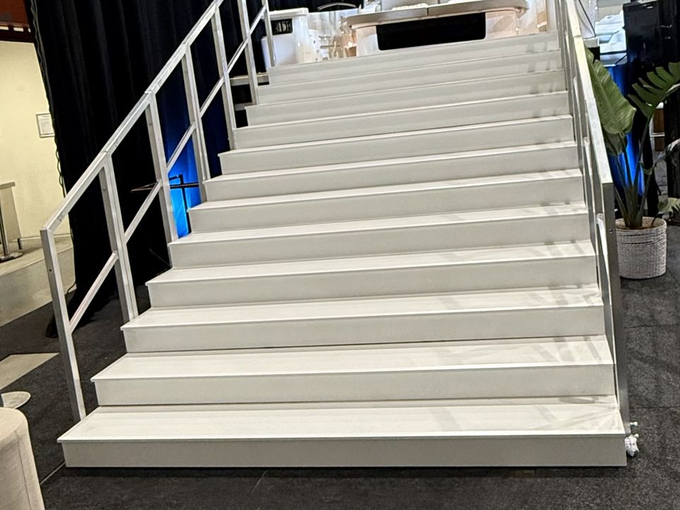 Wide white staircase with handrails leading up to a raised stage