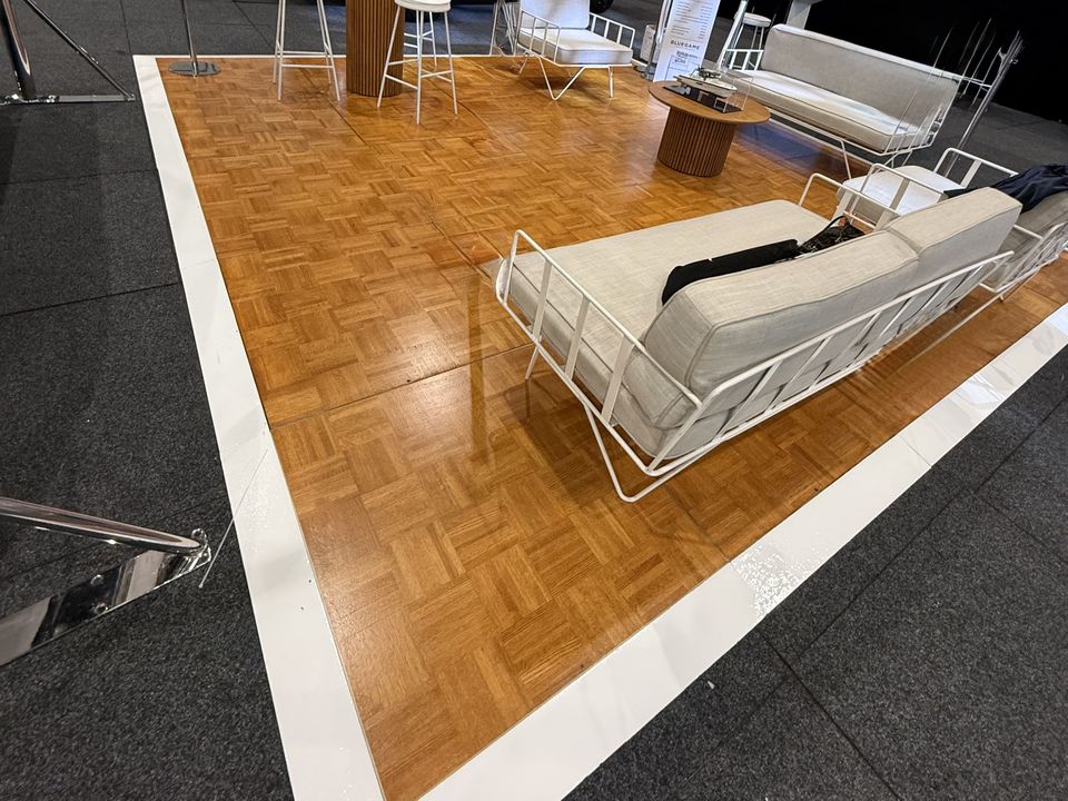Teak dance floor with a white edge, set with lounge furniture at an indoor expo