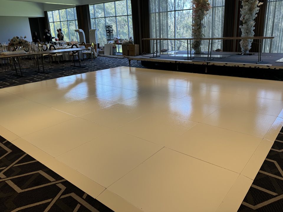 White gloss dance floor in a function room, with a stage and tall floral displays behind