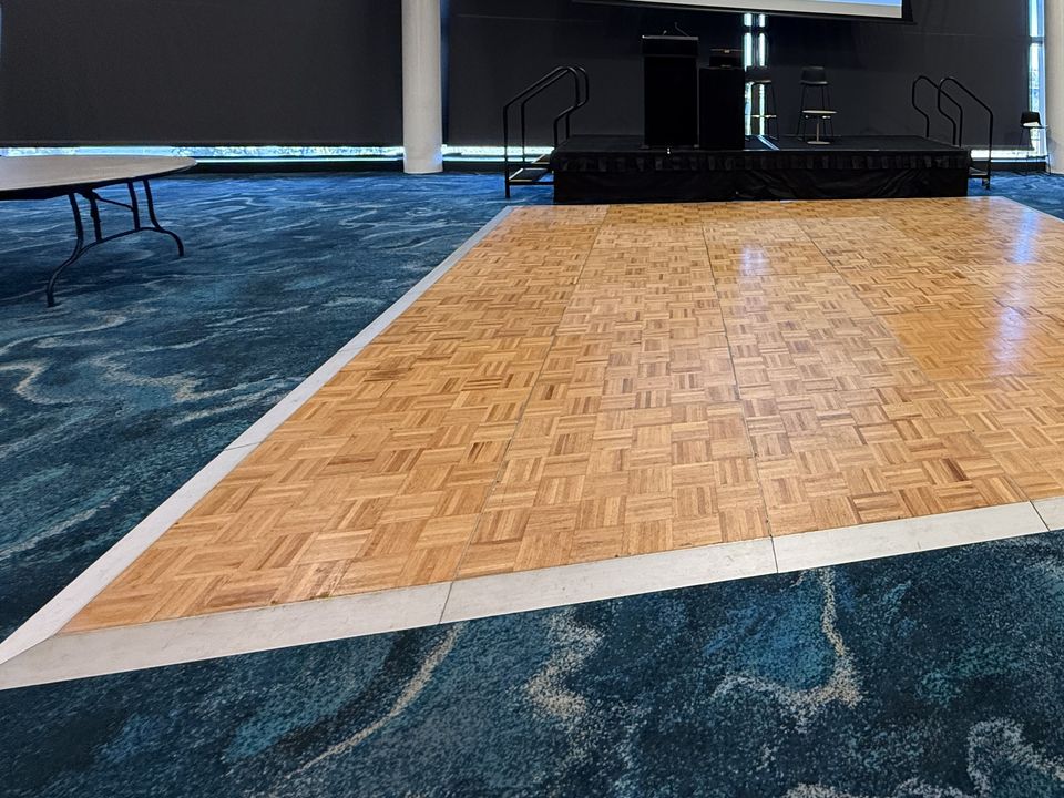Parquetry dance floor with white edging on blue patterned carpet in a function room, with a low stage behind