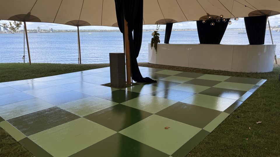 Green checkered dance floor on grass under a sailcloth tent beside the river