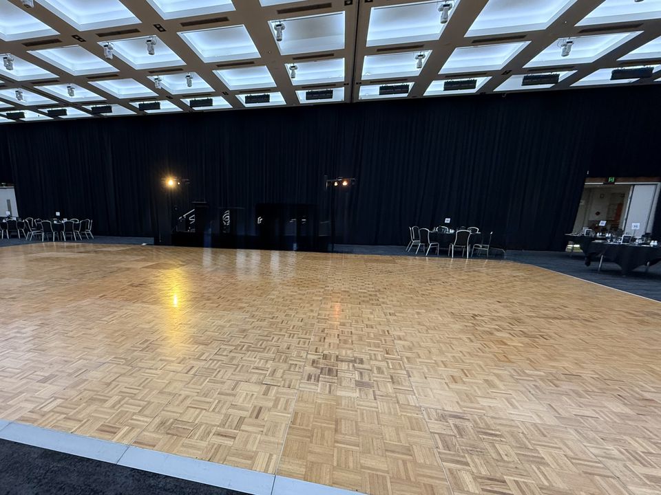 Parquetry dance floor with white edging in a large function room with black drapes