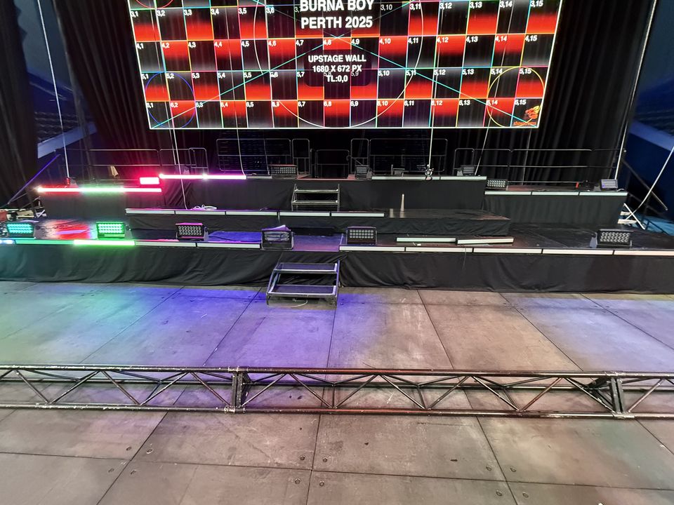 Multi-level black concert stage with coloured LED edge lighting and step units, in front of a large LED screen