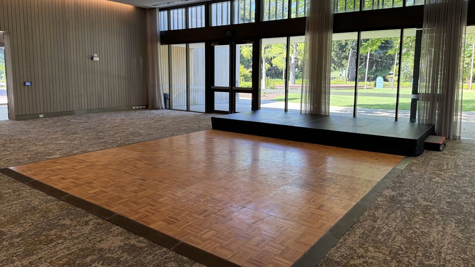 Parquetry dance floor set up in front of a black stage in a function room with tall windows
