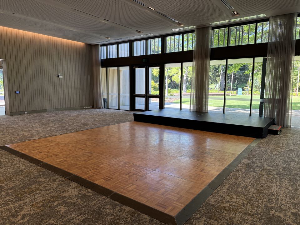 Parquetry dance floor with black edging in a function room with floor-to-ceiling windows and a stage behind