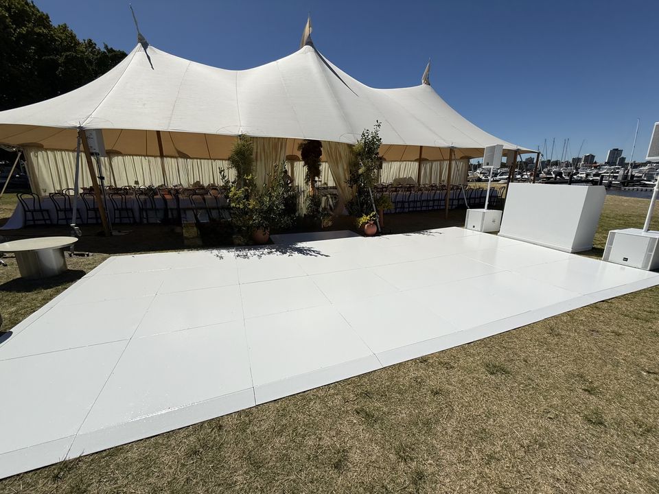 White dance floor on grass in front of a sailcloth tent
